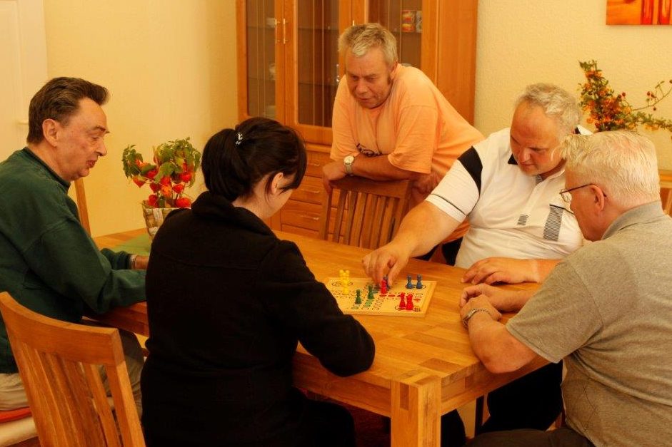 Horizonte e.V. betreutes Gruppenwohnen Fünf Personen spielen ein Brettspiel am Tisch in einem gemütlichen Raum.